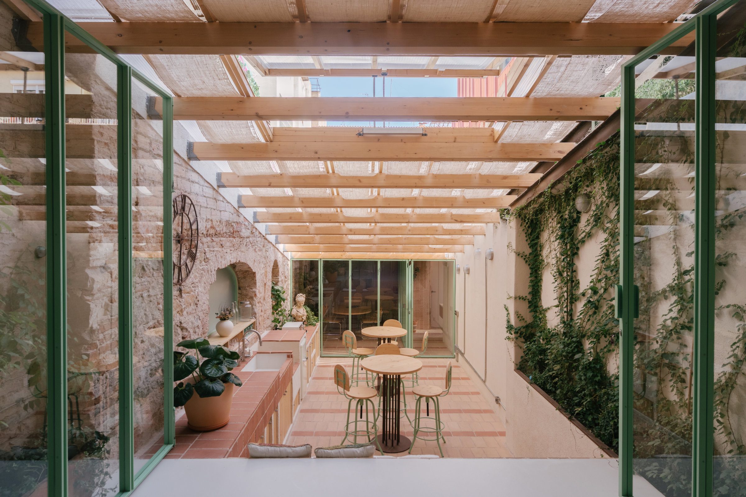 rehabilitacion-vivienda-edificio-existente-barcelona Patio contemporáneo en rehabilitación de vivienda existente con estructura de madera, vegetación y arquitectura tradicional restaurada